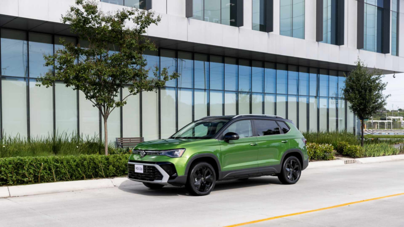 Taos de Volkswagen verde de perfil sobre una avenida, junto a un edificio de oficinas y árboles jóvenes.