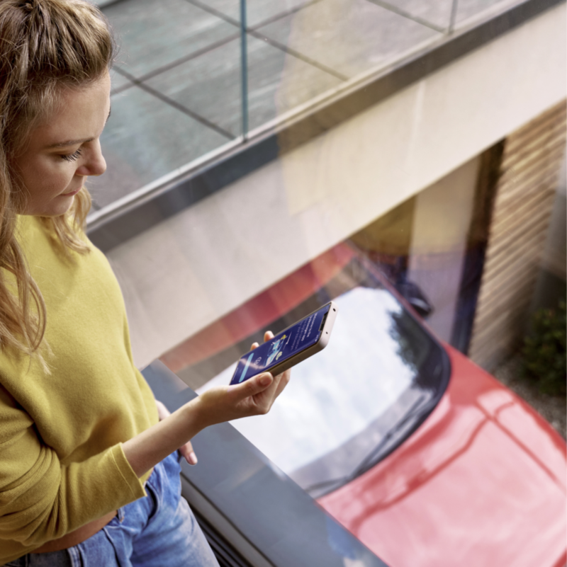 Woman using smartphone to perform over-the-air vehicle software updates.