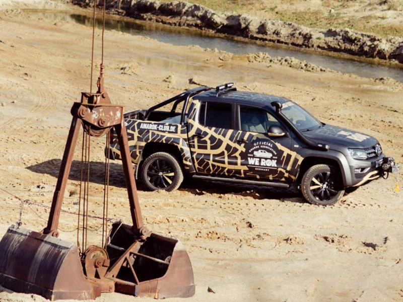 Ein Volkswagen Amarok steht in einer Kiesgrube mit einem Kranbagger im Vordergrund.