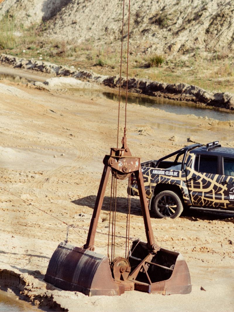 Ein VW Amarok steht in einer Kiesgrube mit einem Kranbagger im Vordergrund.