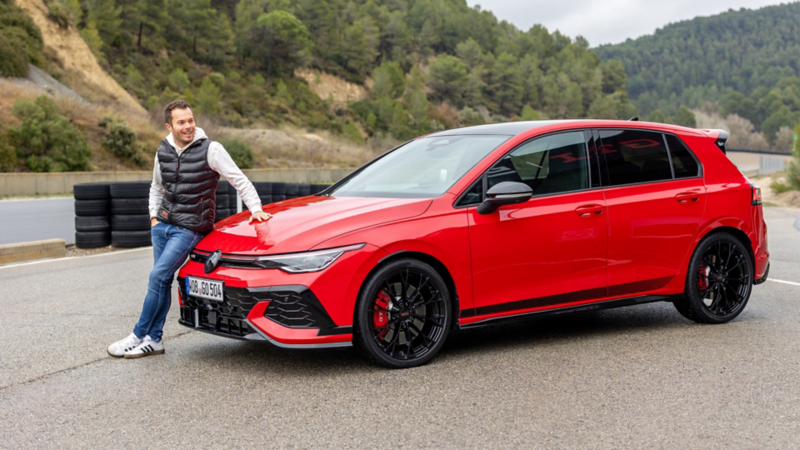 Benjamin «Benny» Leuchter lehnt lässig an einem roten Volkswagen Golf GTI auf einer Rennstrecke.