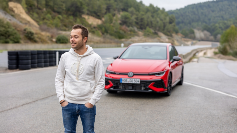 Portrait de Benjamin «Benny» Leuchter sur une piste d’essai avec une Volkswagen Golf GTI rouge en arrière-plan.