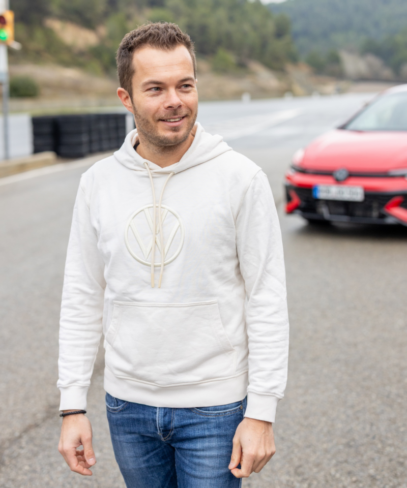Portrait de Benjamin «Benny» Leuchter sur une piste d’essai avec une Volkswagen Golf GTI rouge en arrière-plan.