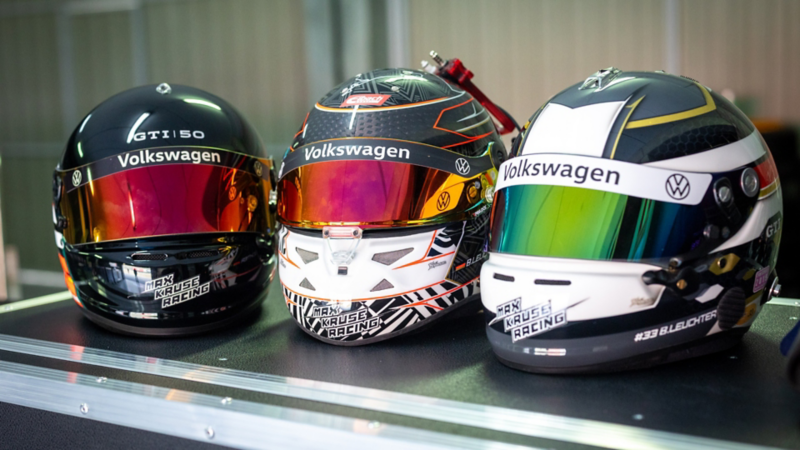 Drei verschiedene Rennhelme von Volkswagen Motorsport liegen nebeneinander auf einem Tisch.
