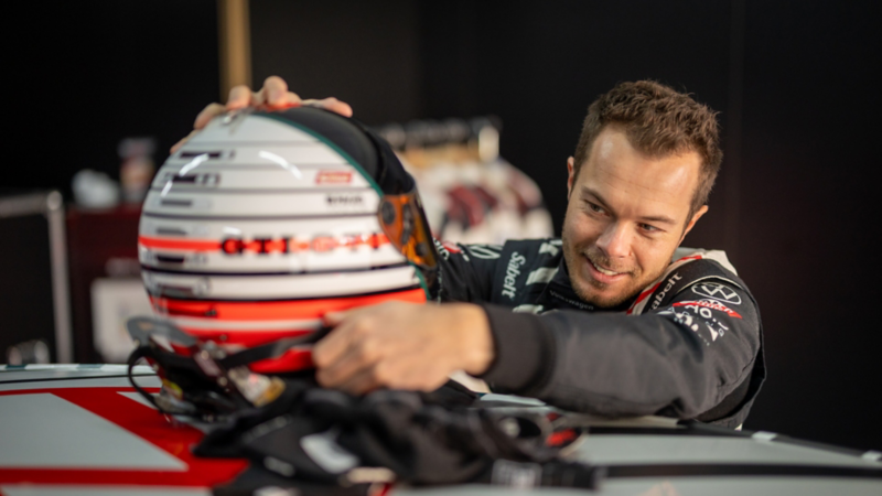 Benjamin «Benny» Leuchter bereitet einen Rennhelm neben einem Volkswagen Rennfahrzeug vorBenjamin «Benny» Leuchter prépare un casque de course à côté d’une voiture de compétition Volkswagen.