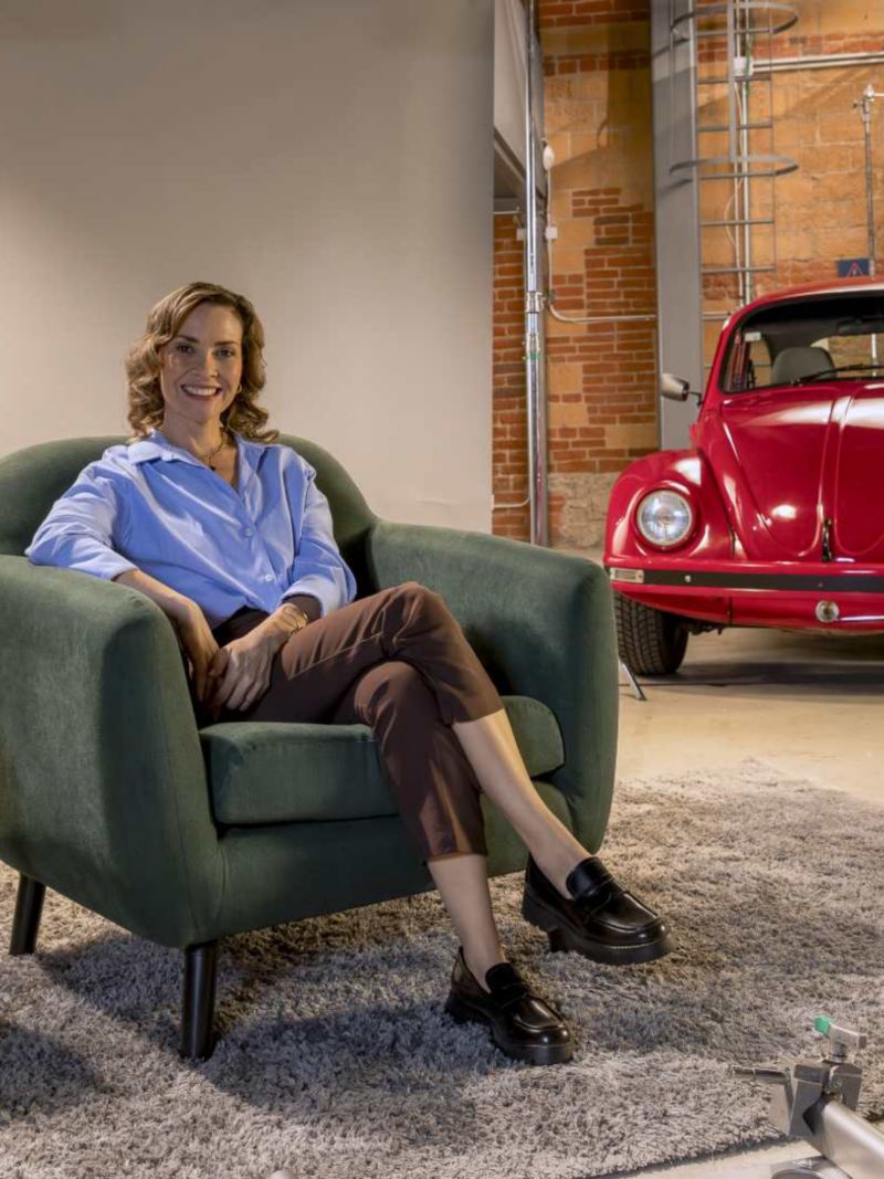 Mujer sentada en sillón comparte experiencia con un Vocho de Volkswagen. 