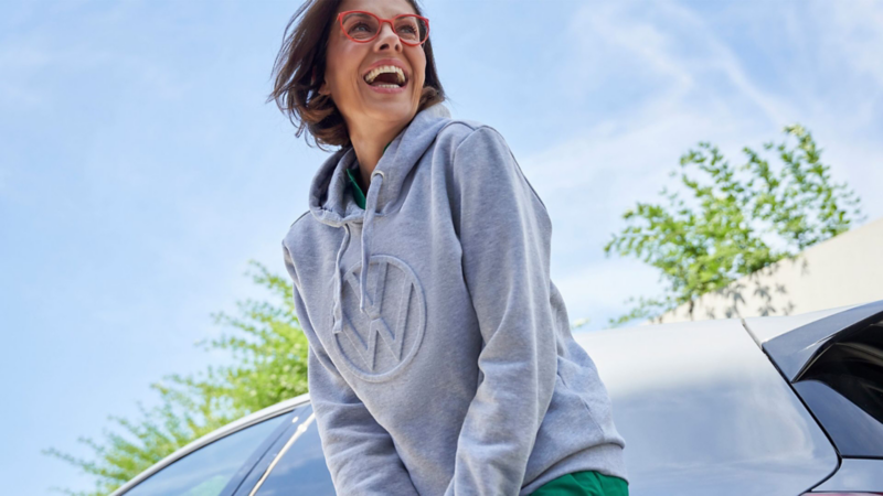Mujer sonriente viste prenda de Volkswagen Collection. Hoodie con logo VW. 