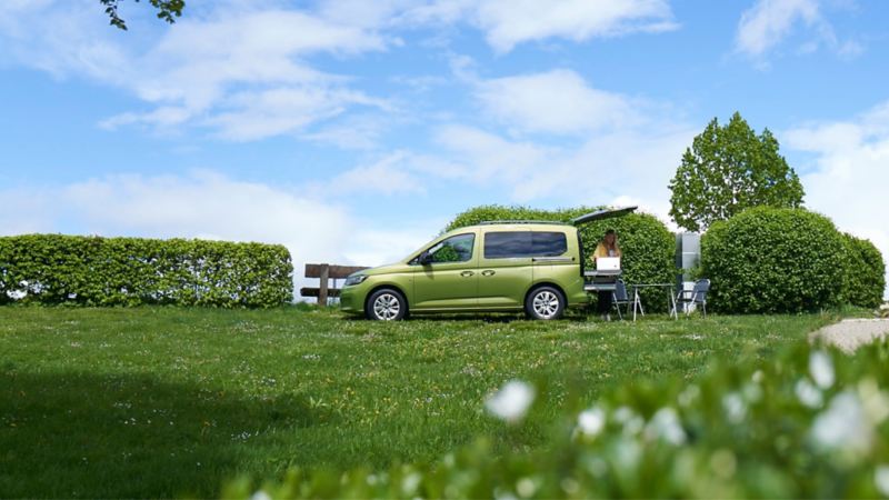 Sidovy av VW Caddy California på en grön äng