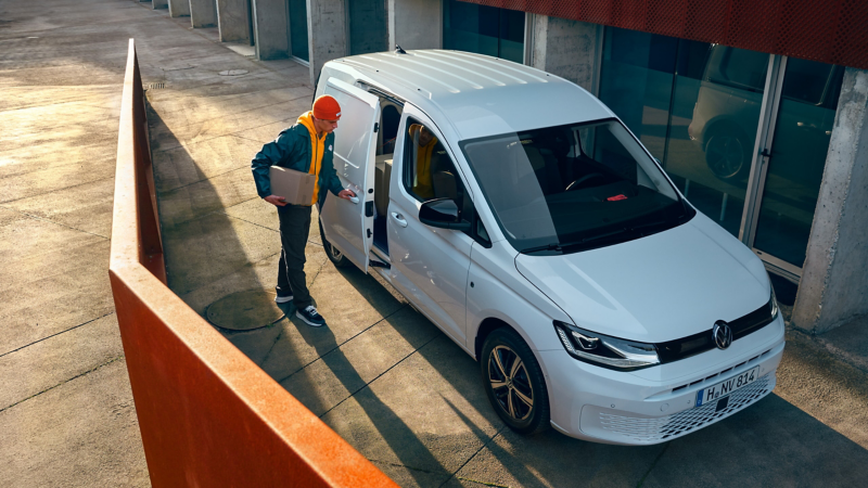 Une personne chargeant un colis dans un Volkswagen Caddy Cargo blanc.