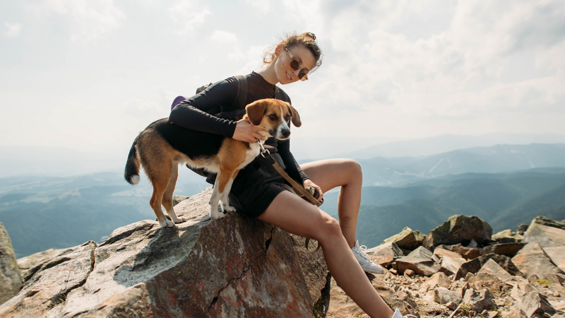 Eine Frau sitzt mit einem Hund auf einem Stein.