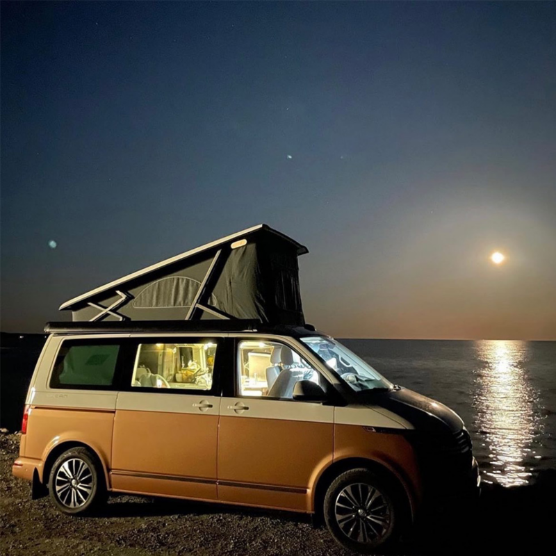 VW California Ocean med uppfällt tak under stjärnhimlen vid havet.