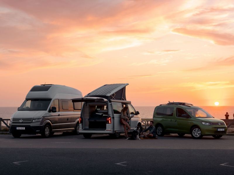 VW California 6.1, VW Caddy California och VW Grand California uppställda på en strand i solnedgång