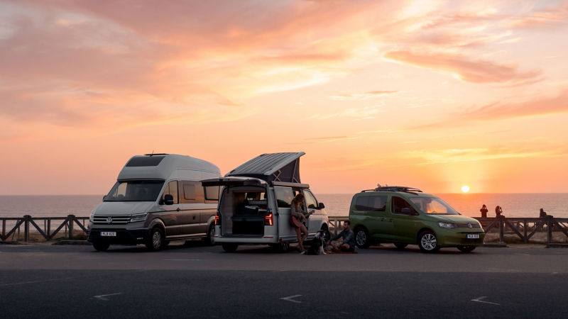 VW California 6.1, VW Caddy California och VW Grand California uppställda på en strand i solnedgång