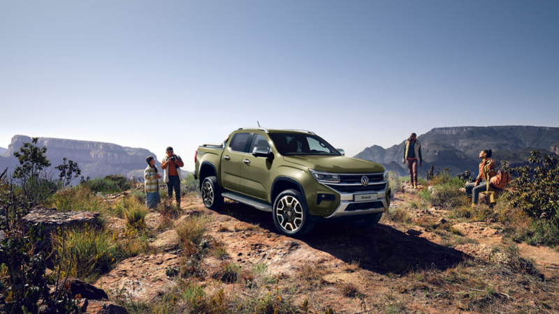 Camioneta Volkswagen Amarok color verde olivo en terreno montañoso con personas admirando el paisaje.