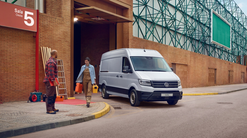 Volkswagen Crafter blanco estacionado frente a edificio industrial. Mujer con maletín camina hacia hombre.