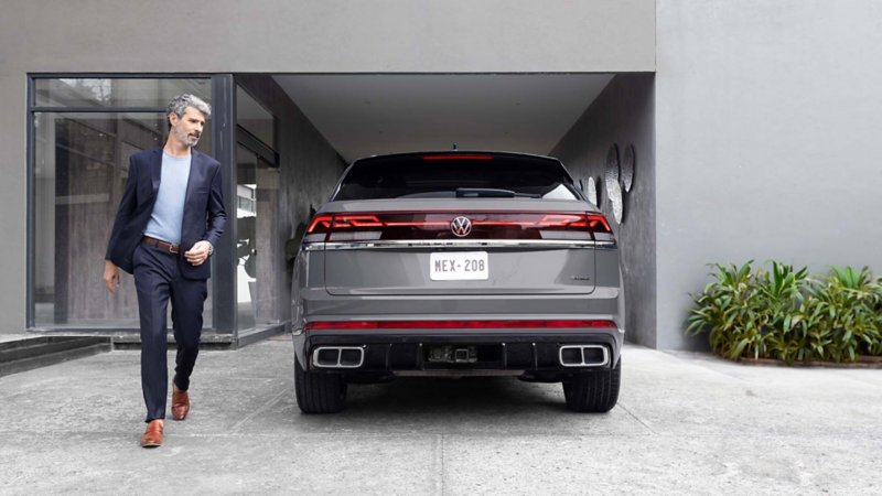 Hombre camina a lado de una camioneta Cross Sport 2026 de color exterior gris, con un par de escapes y gancho para remolques. 