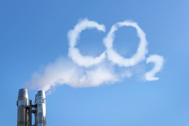 Rauch steigt aus zwei Industrieschornsteinen zu einer Wolke auf, die das Wort “CO2” formt.