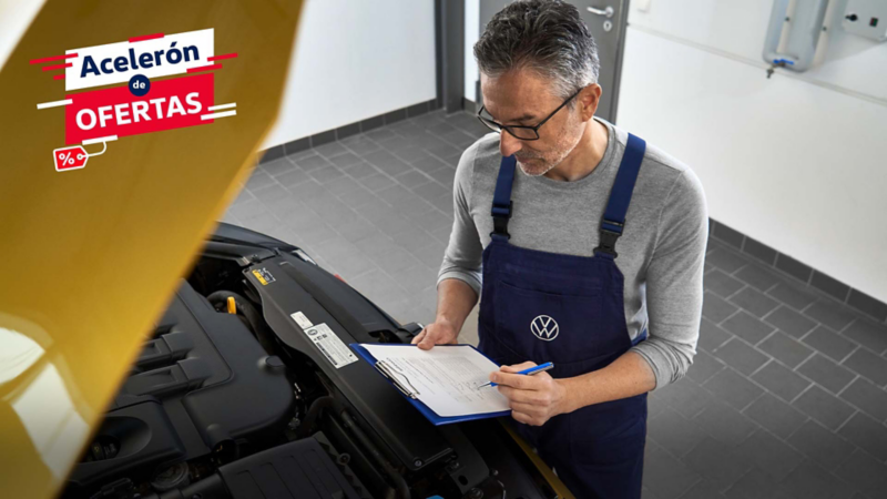 Técnico Volkswagen revisa motor con portapapeles en taller de servicio autorizado.