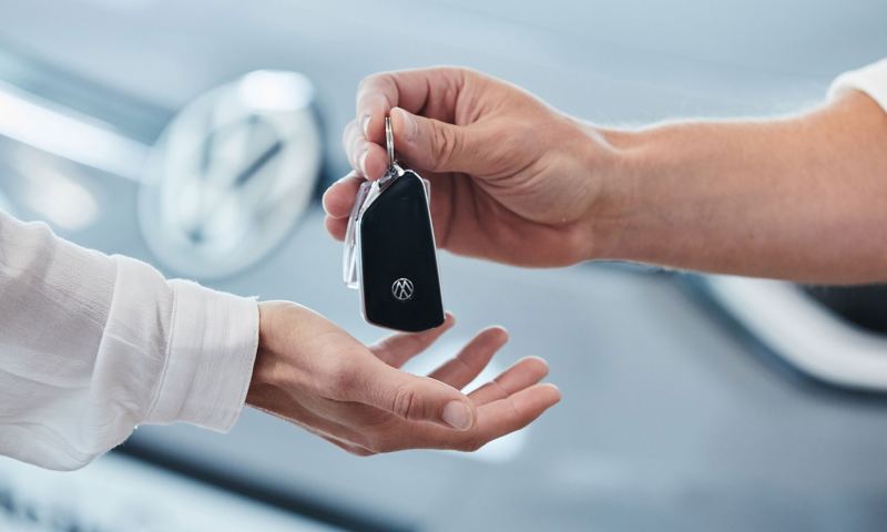 Eine Hand übergibt einem Kunden den Schlüssel zu seinem neuen Elektroauto.