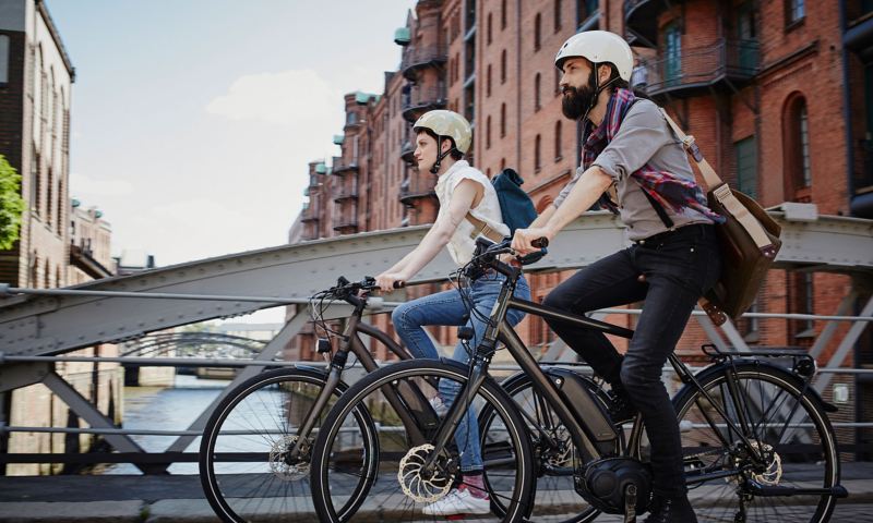 Eine Radfahrerin und ein Radfahrer fahren auf E-Bikes über eine Brücke
