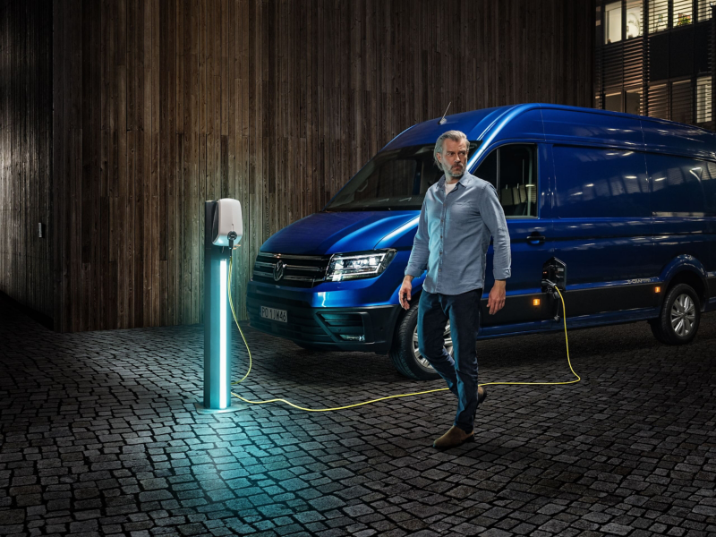Mężczyzna w średnim wieku na tle ładującego się Volkswagena e-Craftera.