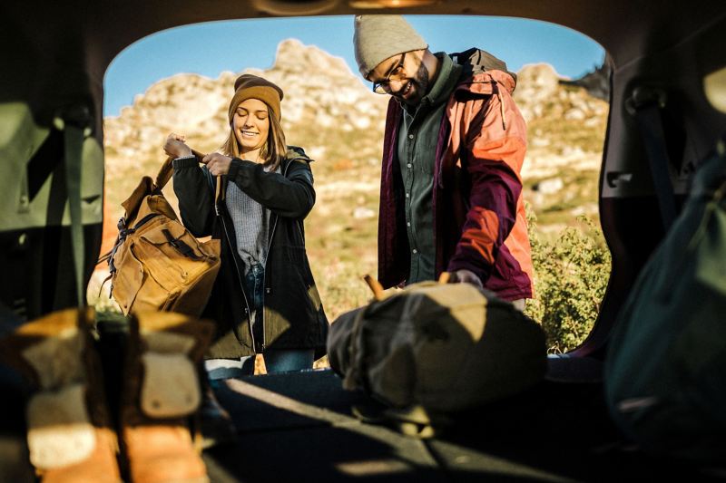 Ein Paar holt ihre Rucksäcke aus dem Kofferraum eines Autos, das bei schönem Wetter in der Nähe der Berge parkt.