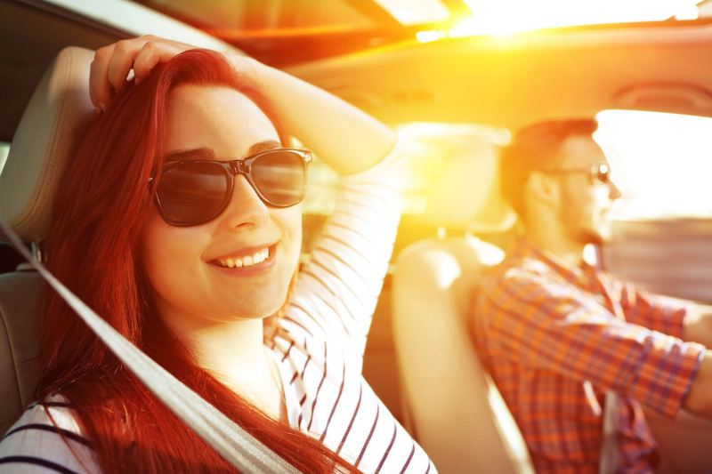 Ein Paar fährt im Sommer mit einem Auto, die Sonne scheint durch das offene Schiebedach.