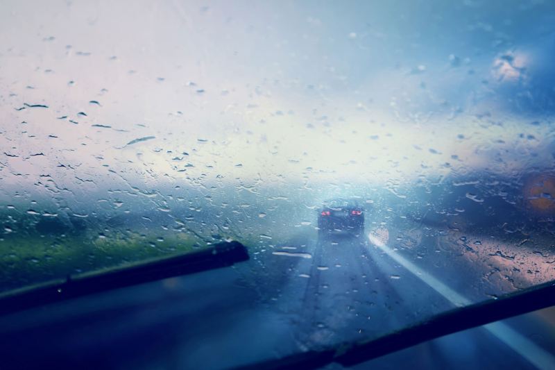Ein Auto unterwegs bei starkem Regen und regennasser Fahrbahn.