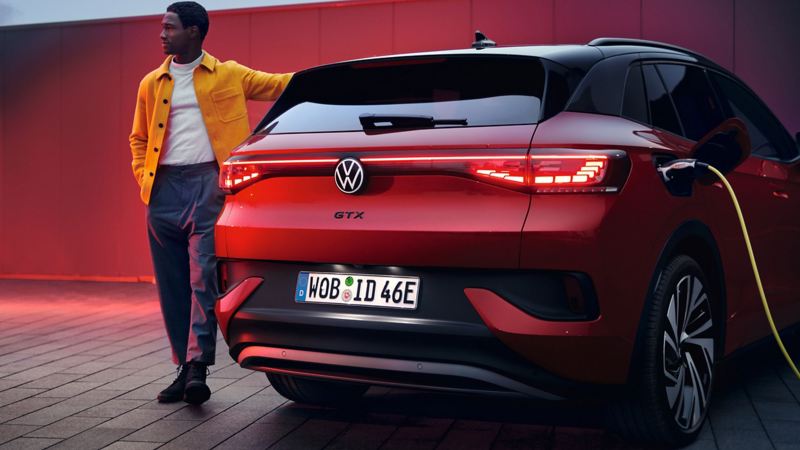 Ein junger Mann lädt seinen roten VW ID. 4 GTX an einer Ladestation.