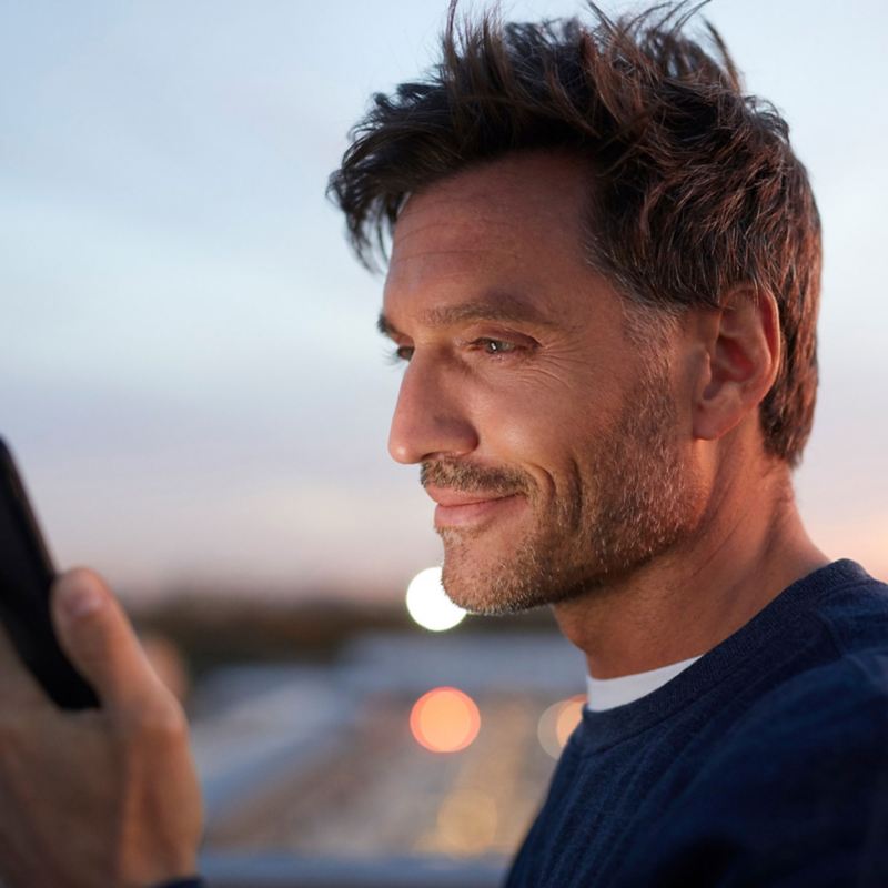 Ein Mann schaut in der Abenddämmerung lächelnd auf sein Smartphone.
