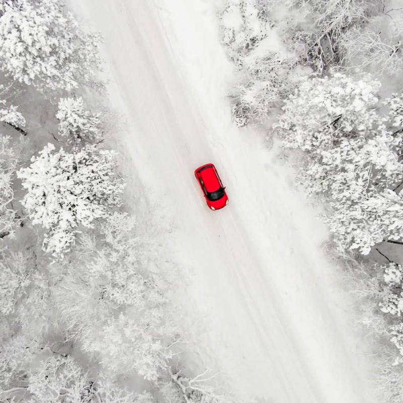 Ein rotes Auto fährt durch eine schneebedeckte Landschaft.