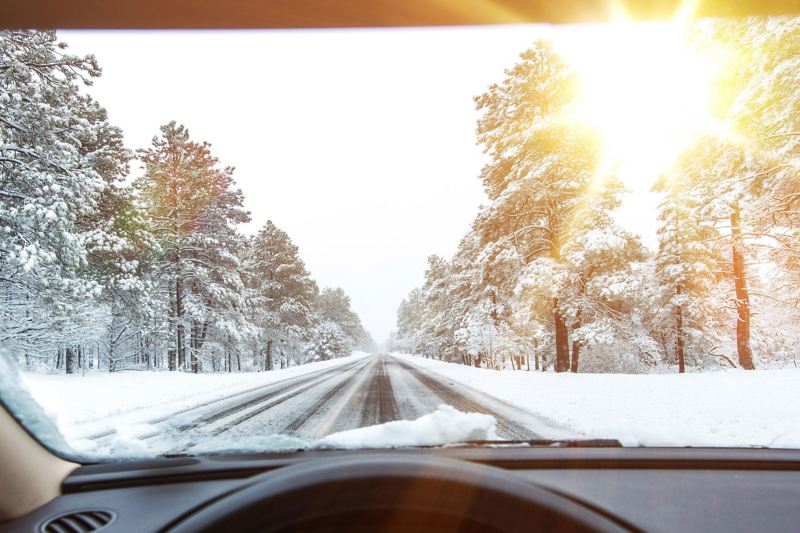 Ein Auto fährt über eine verschneite Straße, auf dem Foto ist die Perspektive des Fahrers oder der Fahrerin zu sehen. 