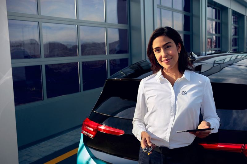 Eine Mitarbeiterin von Volkswagen steht mit einem Volkswagen VW ID.3 und dem Autoschlüssel vor einer Garage.