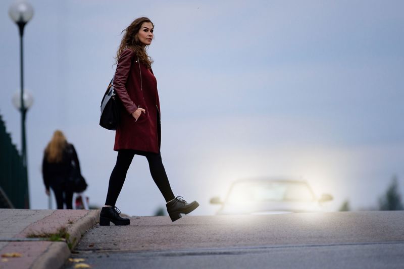 Frau überquert die Straße und schaut nach rechts, im Hintergrund nähert sich ein Auto von links.