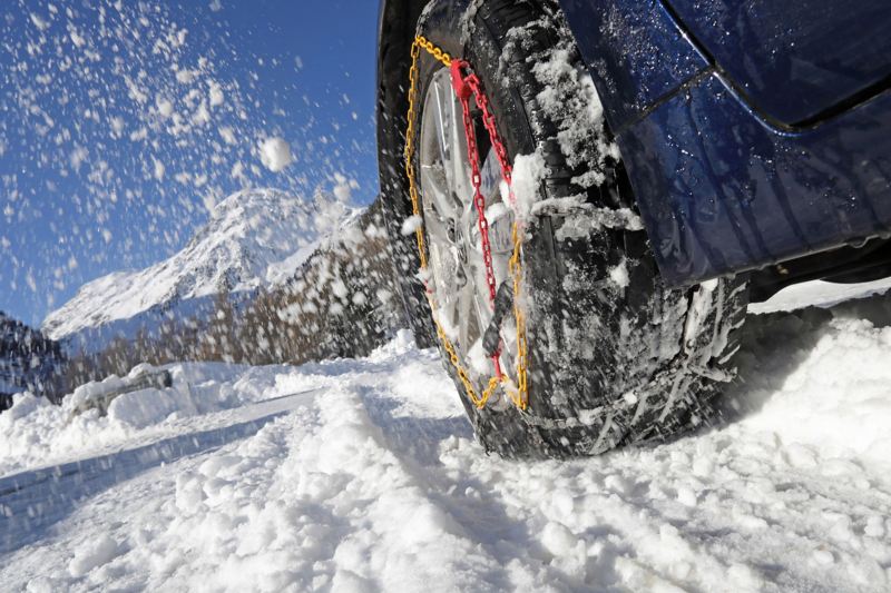 Nahaufnahme von Schneeketten an einem Reifen im Schnee.