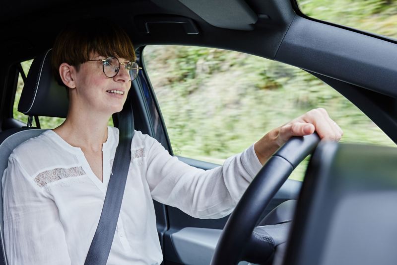 Lächelnde Frau mit Brille am Steuer eines Fahrzeugs.