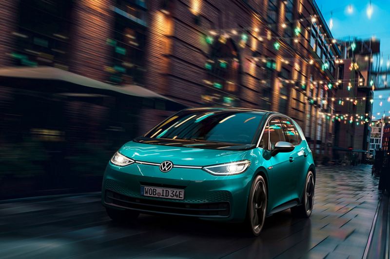 Volkswagen ID.3 (Stromverbrauch kombiniert: 15,6–13,1 kWh/100 km (NEFZ); CO2-Emission kombiniert: 0 g/km; Effizienzklasse: A+) einer Straße, im Hintergrund ein Girlanden und Abendhimmel 