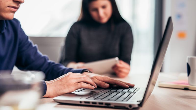 Ein Mann arbeitet am Laptop, eine Frau studiert ein Dokument