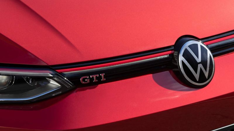 Logo VW en la parte delantera de Golf GTI 2024, modelo deportivo en color rojo.