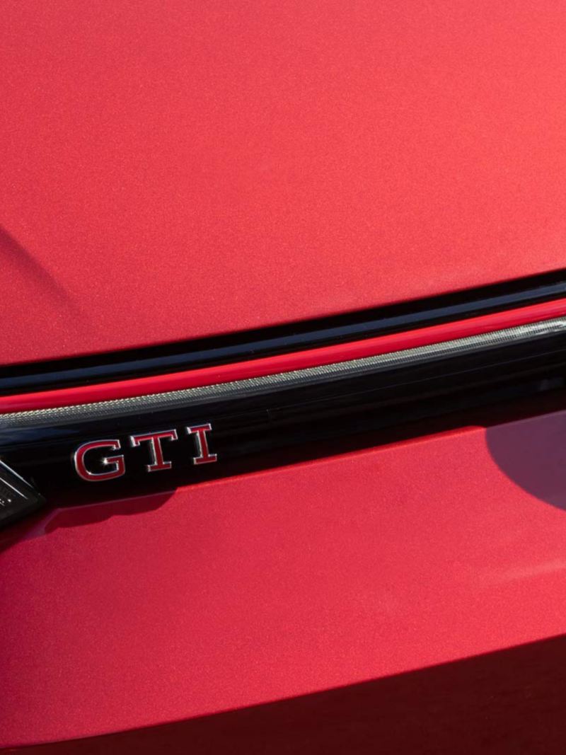 Logo VW en la parte delantera de Golf GTI 2024, modelo deportivo en color rojo.