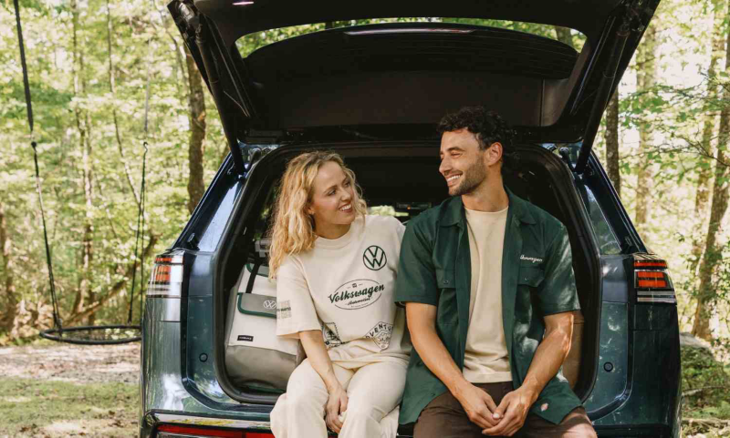 Una pareja sentada en la parte trasera de un Volkswagen rodeada de un bosque.