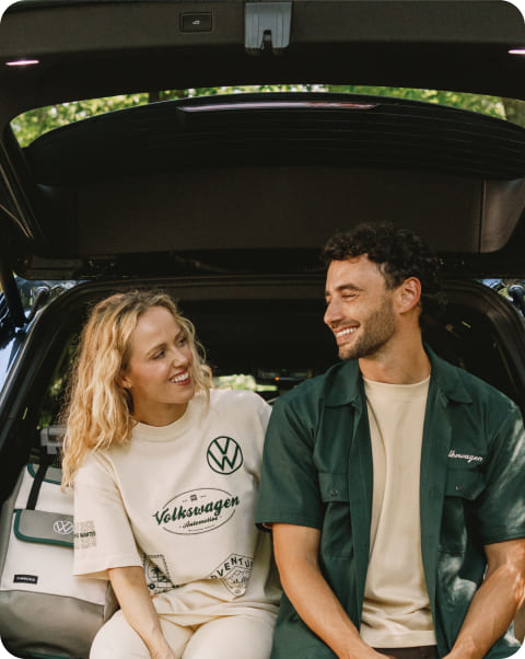 A couple sitting in the back of a Volkswagen vehicle surrounded by a forest.
