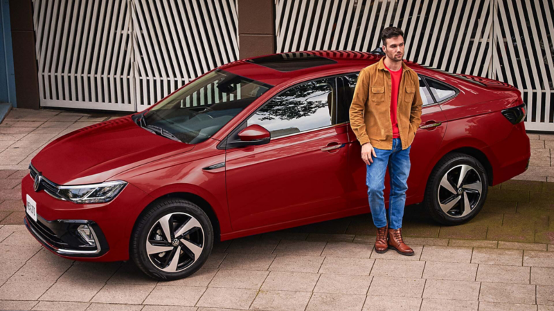 Virtus VW versión Highline en color rojo, con joven conductor recargado en la puerta trasera. 