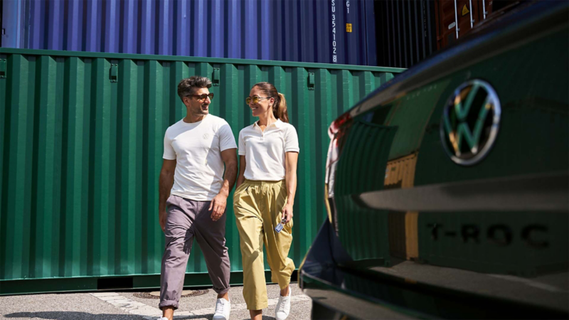 Pareja con camisetas blancas camina junto a un SUV Volkswagen T-Roc verde.
