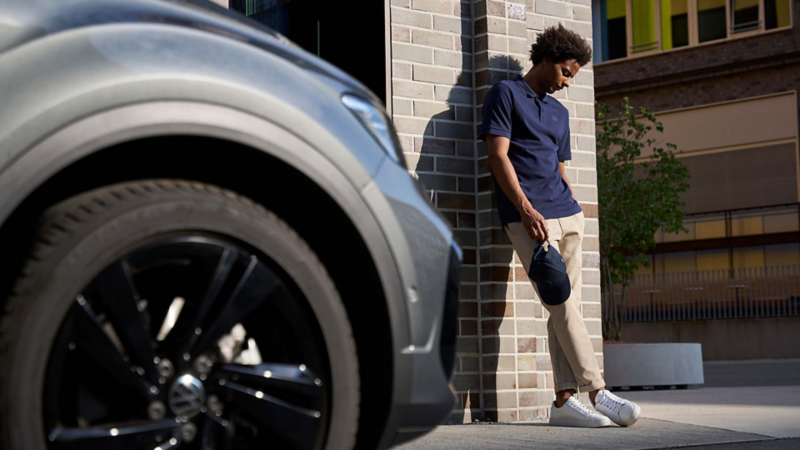 Hombre con polo azul juega con un balón junto a un SUV Volkswagen gris.