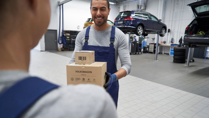 Técnico de Volkswagen carga cajas con refacciones, en el interior de un taller. 