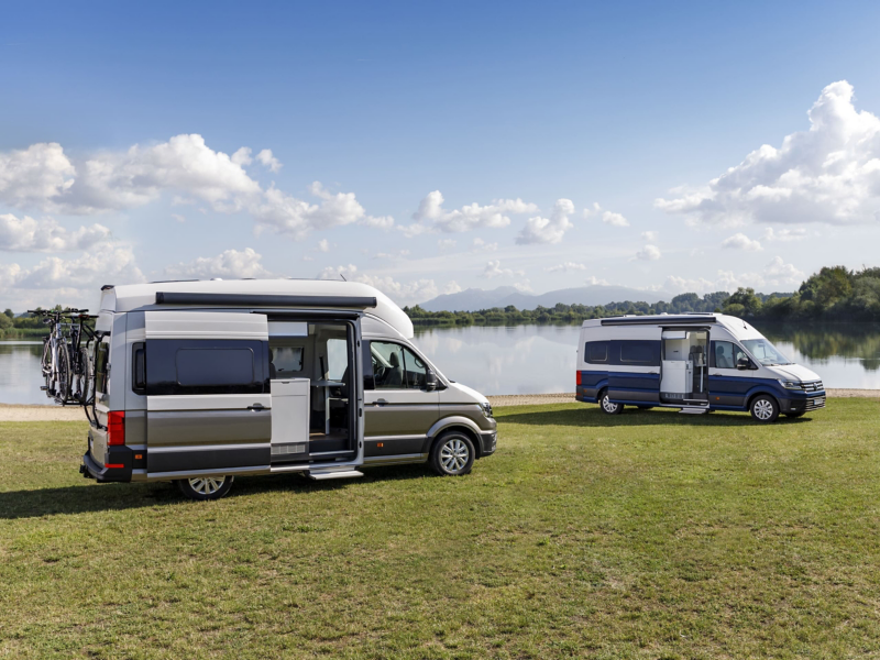 Dwa Volkswageny Grand California stoją na brzegu jeziora. 
