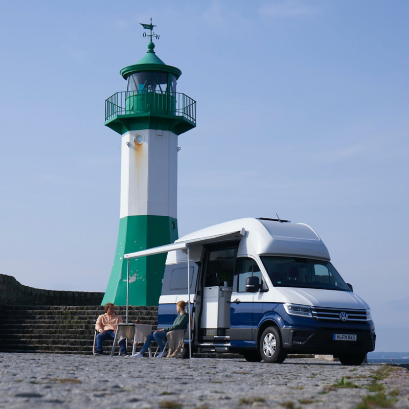 Ein VW Grand California 600 steht vor einem Leuchtturm.