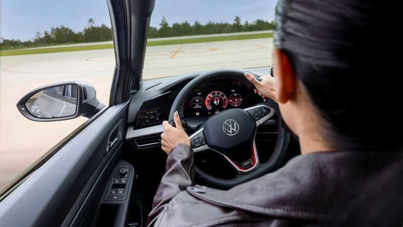 Mujer toma el volante de un Volkswagen deportivo, mientras hace una prueba de manejo. 