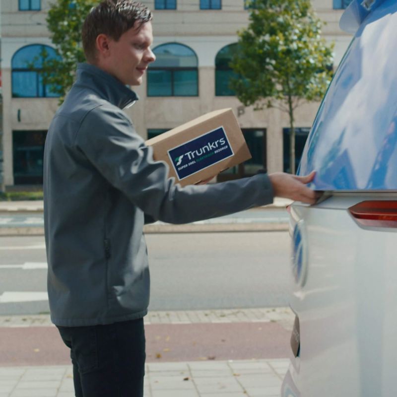 Ein Mann öffnet die Ladeklappe vom VW ID. Buzz mit einem Trunkrspaket in der Hand.